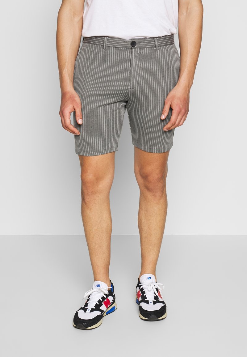 Shorts rayés gris avec une coupe droite, dotés d'une fermeture par bouton et de passants pour ceinture. Portés avec des baskets noires et blanches.