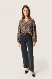 Sort og beige mønstret bluse med V-udskæring og puffede ærmer, parret med høj talje sorte jeans og spidse sorte hæle.