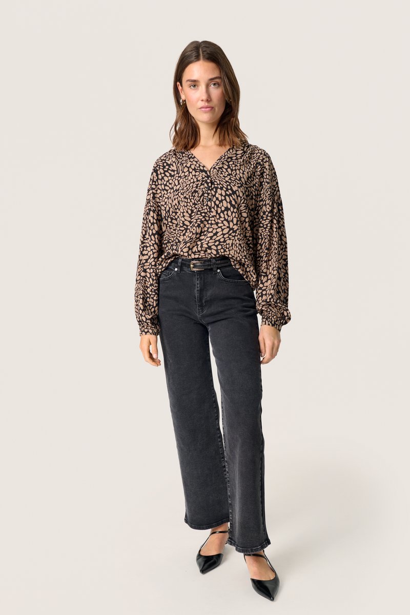 Sort og beige mønstret bluse med V-udskæring og puffede ærmer, parret med høj talje sorte jeans og spidse sorte hæle.
