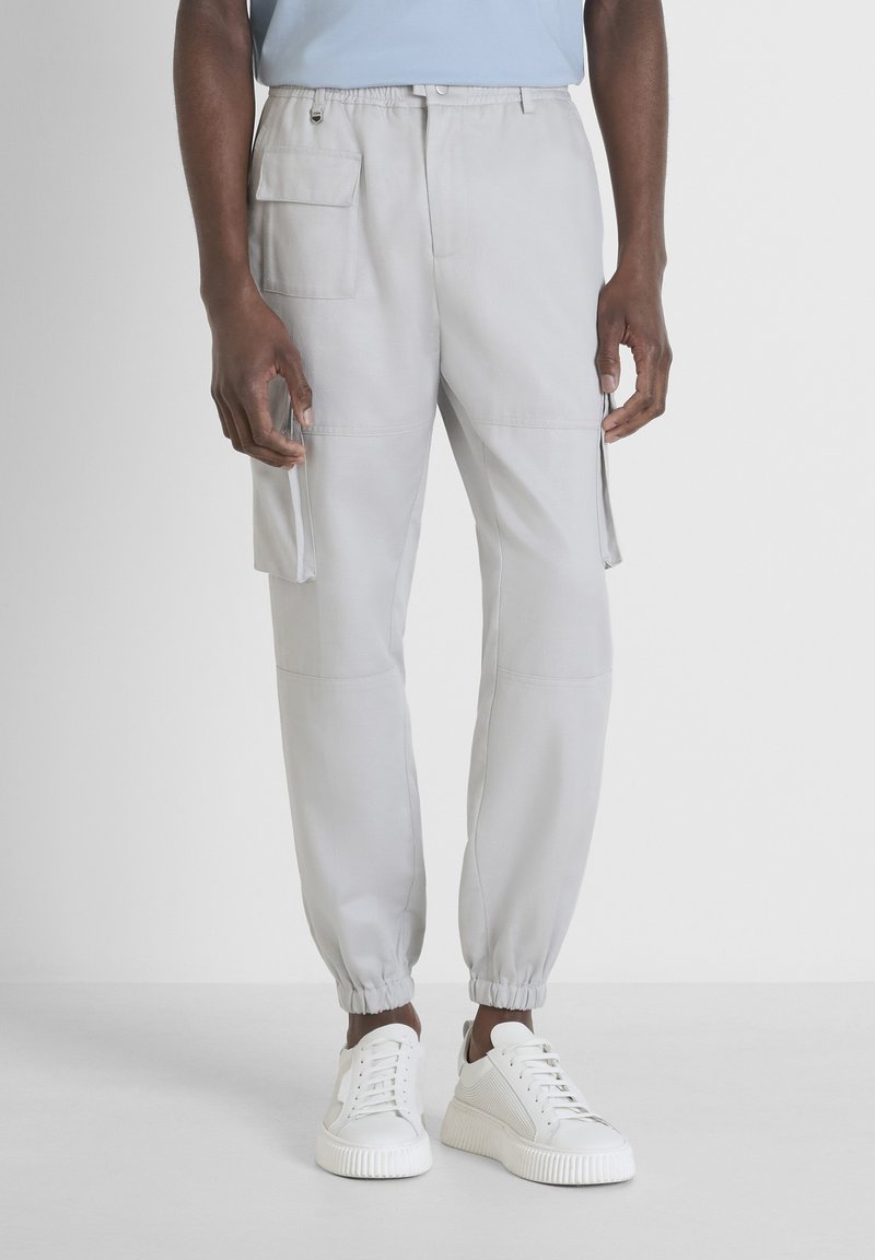 Pantalons cargo gris clair avec une taille élastique, deux poches latérales, des poignets resserrés et un tissu texturé. Associés à des baskets blanches.