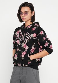 Czarna kwiatowa bluza z kapturem z różowym logo GAP. Z motywem różowych i kremowych róż oraz zielonych liści. Długie rękawy z prążkowanymi mankietami i kieszenią typu kangurka.