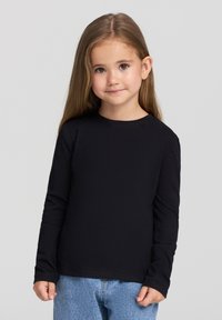 Czarna, długorękawowa bluzka z miękkiego, gładkiego materiału. Posiada okrągły dekolt i dopasowane rękawy, zestawiona z jasnoniebieskimi dżinsami.