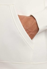 Felpa bianca con cappuccio, dotata di tasca frontale, texture morbida, polsini a costine e finitura liscia. Mano visibile che riposa all'interno della tasca.