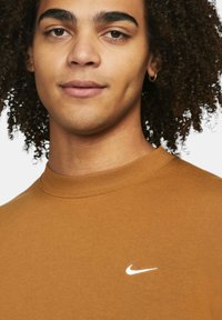 Brun bomulls sweatshirt med rund hals och en vit Nike-logotyp på bröstet, med en slät textur och åtsittande siluett.