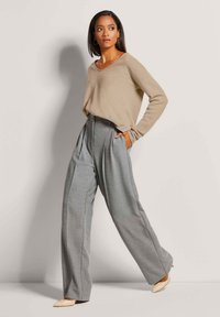 Beiger Pullover mit V-Ausschnitt und langen Ärmeln, kombiniert mit hoch taillierten, grauen, maßgeschneiderten Hosen und beigen spitzen Pumps.