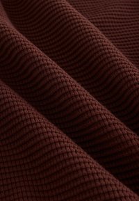 Teksturowana, głęboka karmazynowa tkanina z wzorem kratki, z wyraźnie wypukłymi ściegami tworzącymi fale. Miękka i tkana w dotyku.