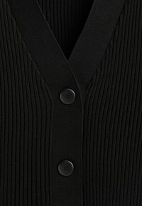 Schwarze gerippte Strickjacke mit V-Ausschnitt und zwei schwarzen Knöpfen vorne, die ein strukturiertes Strickmaterial präsentiert.