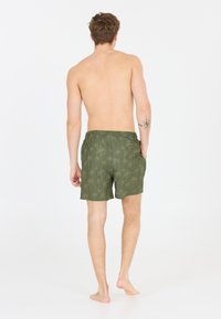 Gröna badshorts med ett palmträdsmönster, elastisk midja och sidofickor. Tyget verkar lätt och slätt.