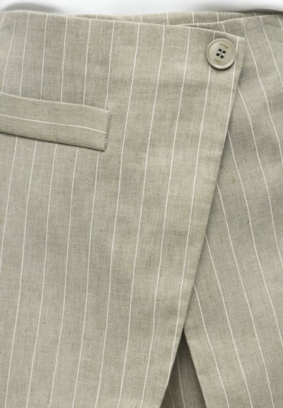 Ύφασμα μπεζ με λεπτές ρίγες, με μπροστινό καπάκι, κούμπωμα με κουμπιά και μικρή οριζόντια τσέπη.