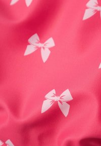 Różowy materiał o gładkiej teksturze z powtarzającym się wzorem białych kokard. Kokardy są wyśrodkowane i symetryczne, co dodaje zainteresowania wizualnego.