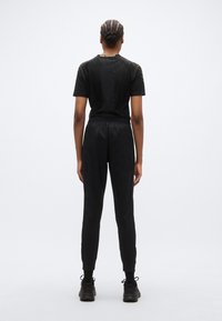 Tenue de sport noire comprenant un haut à manches courtes avec des détails texturés et un pantalon fuselé assorti, tous deux avec une taille et des poignets élastiques.