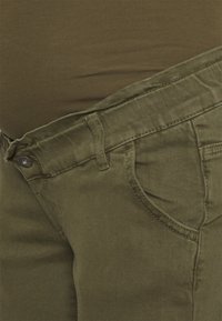 Calças verde-azeitona feitas de um tecido misto de algodão, com um bolso frontal, passantes para cinto e um fecho com botão de metal na cintura.
