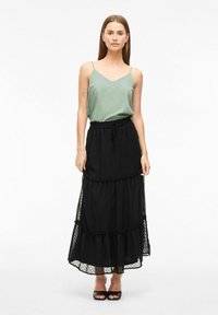 Camisole en satin vert avec de fines bretelles, associée à une jupe maxi noire à pois à plusieurs couches, dotée d'une taille élastique et d'accents volants.