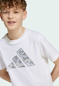 White cotton t-shirt featuring a grey camo pattern logo on the front. Short sleeves and a ribbed crew neck design.