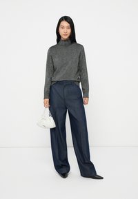 Top de gola alta metálico cinza, calças largas de ganga escura, e pequena mala branca plissada. Modelo a usar sapatos pretos de bico.