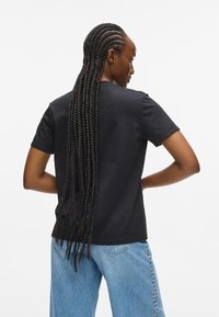 Sort kortærmet t-shirt med rund halsudskæring, lavet af bomuld, kombineret med lyseblå jeans med dekorativ syning langs sømmen.