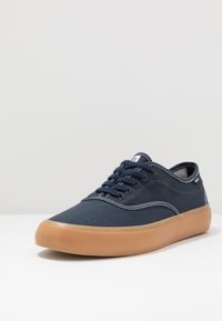 Sneakers in tela blu navy con cuciture bianche, punta rotonda e suola in gomma beige. Caratterizzati da cinque fori e un design a profilo basso.