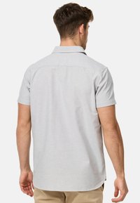 Camisa de manga corta con cuello en mezcla de algodón gris claro, con una textura suave y un dobladillo curvado, vista desde la parte posterior.
