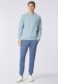 Felpa azzurra chiara a girocollo con polsini a coste, abbinata a pantaloni jogger blu scuro. Entrambi realizzati in tessuto morbido, indossati con sneakers bianche.