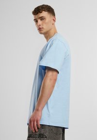 T-shirt en coton bleu clair avec une coupe décontractée, des manches courtes et un col ras du cou. Présente une texture lisse et un design simple.