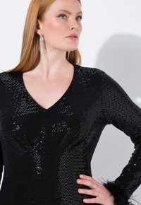 Robe noire en sequins avec un décolleté en V et des manches longues, arborant un design texturé et des accents en fourrure aux poignets.
