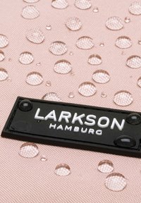 Vesitiivis roosa kangas koos tilkadega; esiküljel must LARKSON Hamburgi logo silt. Tekstuur on kudumis- ja veidi läikiv.