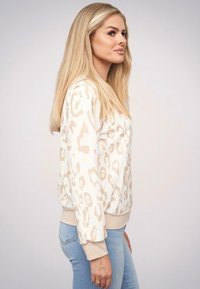 Bluza w panterkę w kolorze kremowym i beżowym, z okrągłym dekoltem, prążkowanymi mankietami i luźnym krojem, połączona z jasnoniebieskimi dżinsami.