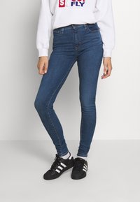 Smaljeans i mörkblå denim, hög midja med en jämn yta och minimal sömnad. Matchade med svarta sneakers med vita ränder.