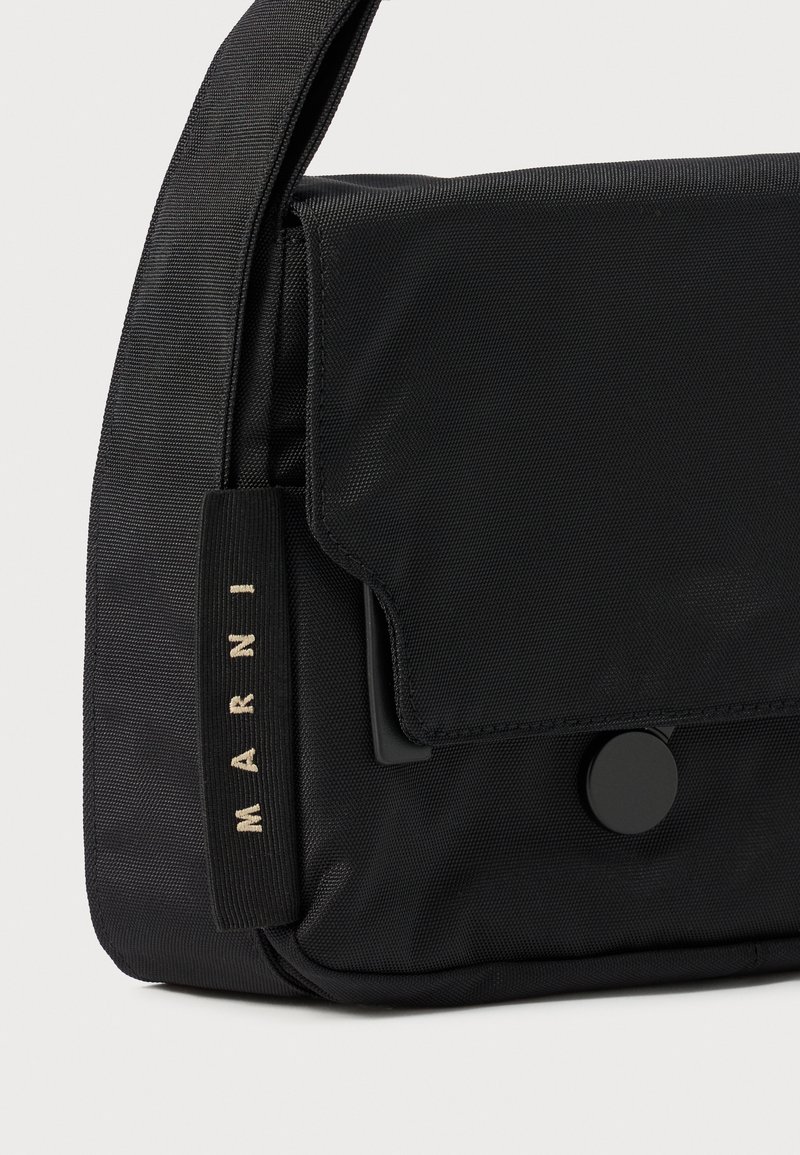 Schwarze Nylon-Crossbody-Tasche mit Klappenverschluss, ausgestattet mit einem Druckknopf, Logolabel und einer beschichteten Textur. Kompaktes und rechteckiges Design.