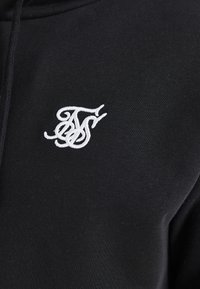 Un sweat à capuche noir en tissu texturé, avec un logo brodé blanc sur la poitrine gauche. Design classique à capuche avec une finition douce.