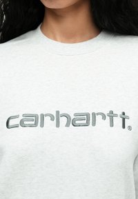 Szary sweter z okrągłym dekoltem, z wyszywanym słowem "carhartt" w ciemnoszarym kolorze na przodzie. Miękka tekstura materiału.