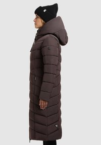 Brown long padded coat with a hood, featuring a chevron pattern, zip closure, and black accents. Worn with a black knit beanie.