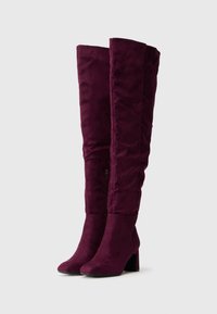 Cizme bordo peste genunchi din suede moale, cu toc bloc și fermoar pe lateral, având un design structurat și ajustat.