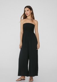 Mono negro sin tirantes con un cuerpo entallado y un corte de pierna ancha, que presenta una cintura fruncida y una tela ligera.