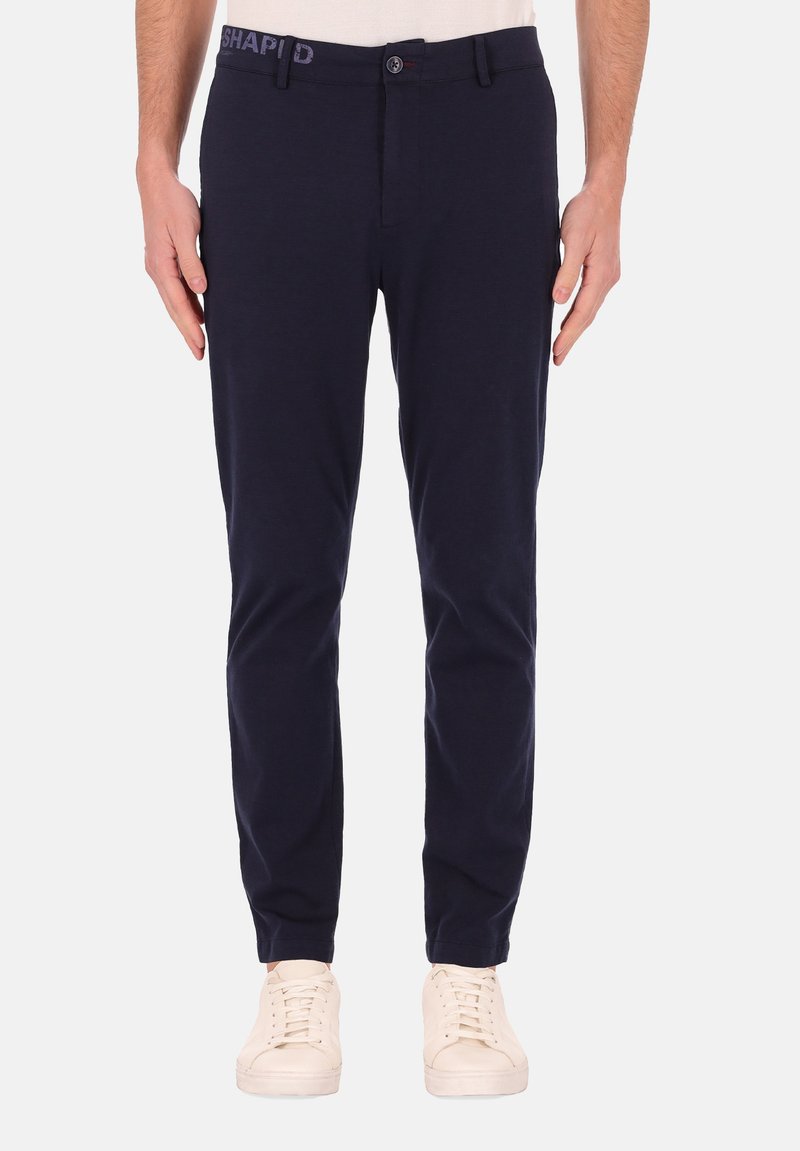 Navyblauwe katoenen broeken met een slim fit, voorzien van een knoopsluiting en geborduurde tailleband, gecombineerd met lichtkleurige sneakers.