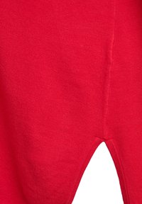 Makro záber červenej pletenej látky s malým trojuholníkovým výrezom a viditeľným švom na pravej strane.