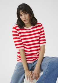 Rød og pink stribet t-shirt med kort ærme og rund halsudskæring, sat mod en ensfarvet baggrund. Båret med lyseblå jeans.
