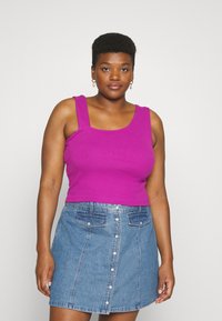 Top com ajuste justo em tecido canelado roxo vivo com alças largas, combinado com uma saia de ganga azul clara com fecho de botões na frente e bolsos.