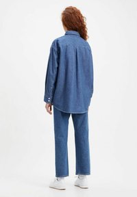 Chemise en denim à manches longues, avec un col et des poignets boutonnés. Associée à un pantalon en denim assorti à jambes droites et des baskets blanches.