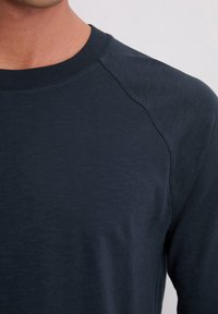 Blauwe lange mouw shirt met een ronde hals en raglanmouwen. De stof lijkt zacht met een subtiele textuur en een lichte glans.