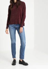 Jersey de punto burdeos con mangas largas y bajo acanalado, combinado con vaqueros rectos de pierna en azul claro y mocasines negros.