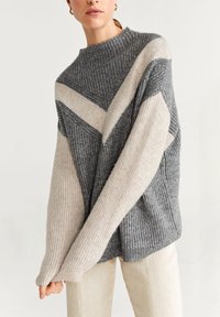 Pull en tricot avec un col haut, présentant des rayures diagonales grises et beiges. Texture douce, coupe oversize et manches longues.