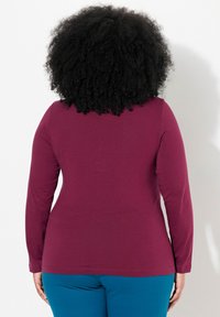 Long-sleeve top in dark burgundy, made from soft fabric. Features a fitted silhouette and rounded neckline. Suitable for casual wear.