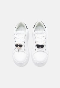 Białe skórzane trampki z fakturowaną podeszwą. Posiadają czarne akcenty i unikalne ozdoby na sznurówkach przypominające postać w okularach przeciwsłonecznych.