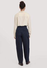 Beige langhalige shirt met een rugpand, gecombineerd met marineblauwe cargobroeken met zakken en een relaxte pasvorm. Donkere schoenen maken de outfit af.