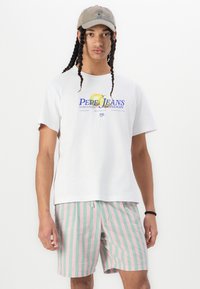 T-shirt blanc à manches courtes avec un logo coloré ; shorts à rayures pastel en rose et vert ; casquette décontractée au design minimal.