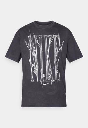 T-shirt di cotone nera con grande logo bianco "NIKE" con un design a fulmine. Maniche corte, scollo rotondo e vestibilità comoda.