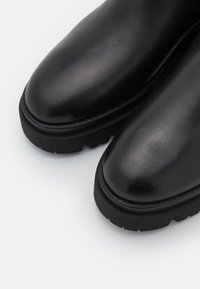 Botas de tobillo de cuero negro con acabado suave, puntera redondeada y suela de goma texturada y gruesa. Presentan costuras limpias y sin herrajes visibles.