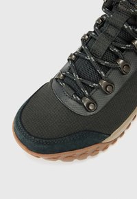 Close-up of a hiking shoe featuring a textured black fabric upper, metal eyelets, and a rubber sole with distinct tread pattern.