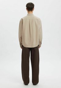 Lys beige skjorte med knapper, med vertikale striper, lange ermer og en avslappet passform, kombinert med løse brune bukser. Minimalistisk design, uten mønstre.